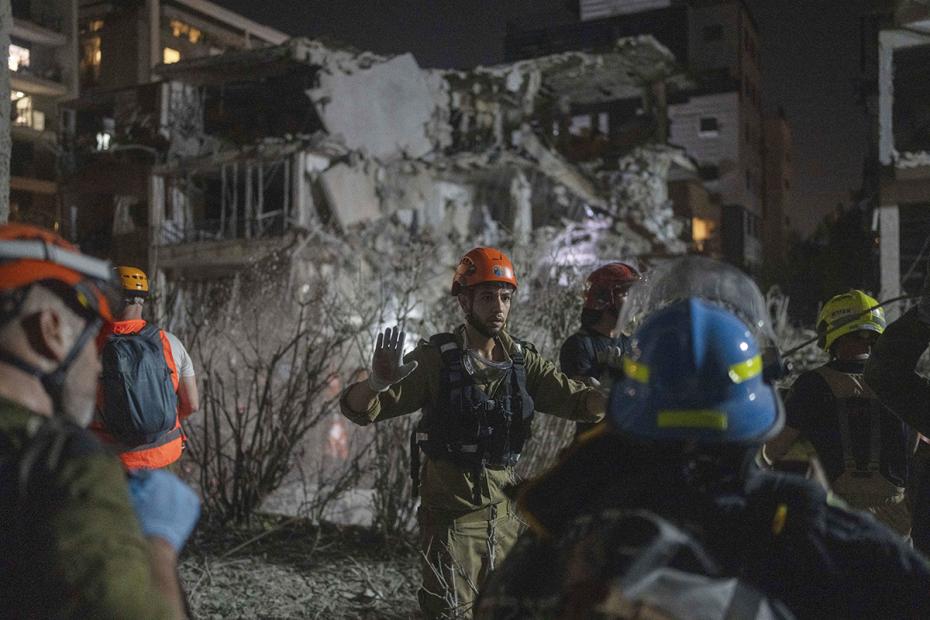 Израильские спасатели и пожарные осматривают последствия ракетного удара в Рамат-Гане