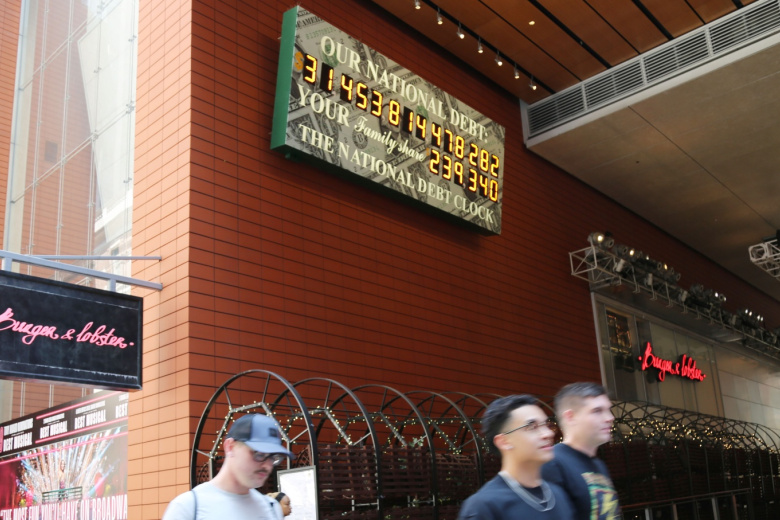 Пешеходы проходят мимо часов государственного долга на Манхэттене, 2023 год
