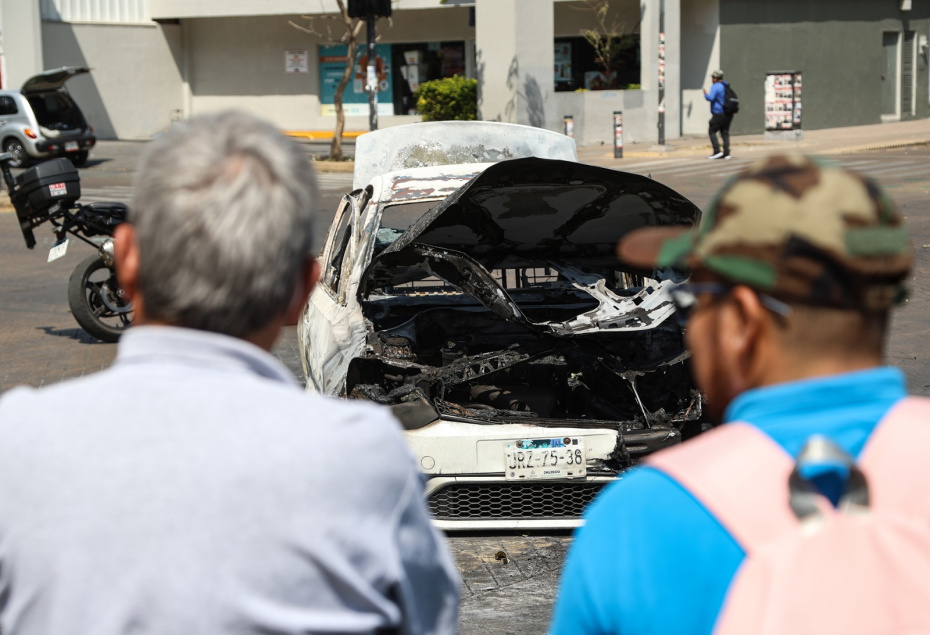 Люди стоят возле сгоревшего автомобиля на улице в Гвадалахаре, столице штата Халиско, Мексика