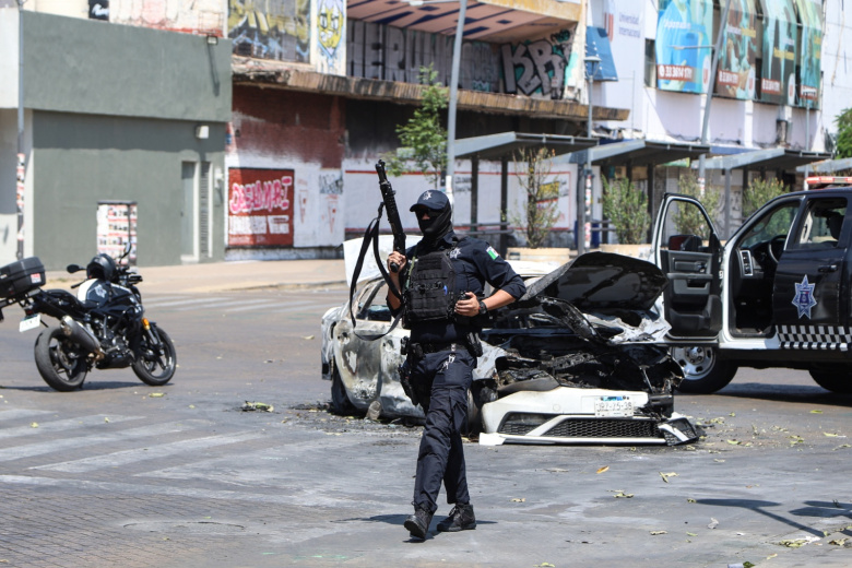 Полицейский дежурит возле сгоревшего автомобиля на улице в Гвадалахаре, столице штата Халиско, Мексика
