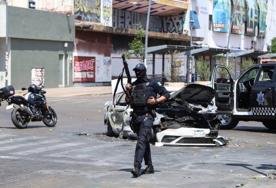 Полицейский дежурит возле сгоревшего автомобиля на улице в Гвадалахаре, столице штата Халиско, Мексика