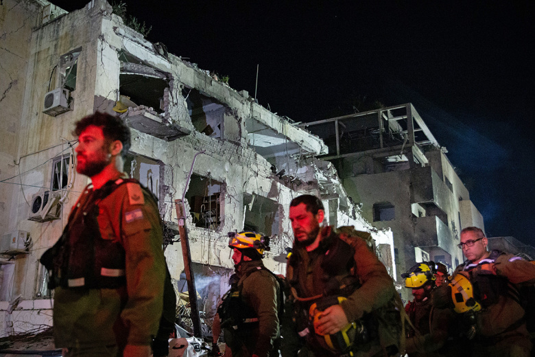 Сотрудники израильских спасательных служб работают на месте попадания баллистической ракеты в Тель-Авиве