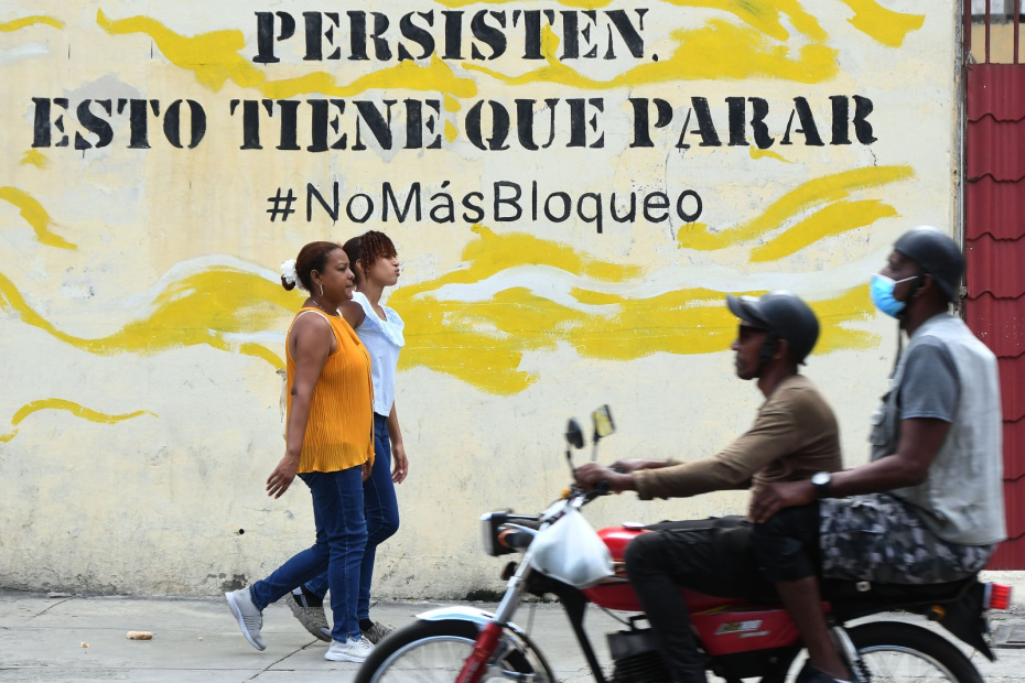 Пешеходы проходят мимо настенной росписи, осуждающей экономическую блокаду Кубы со стороны США, Гавана, Куба