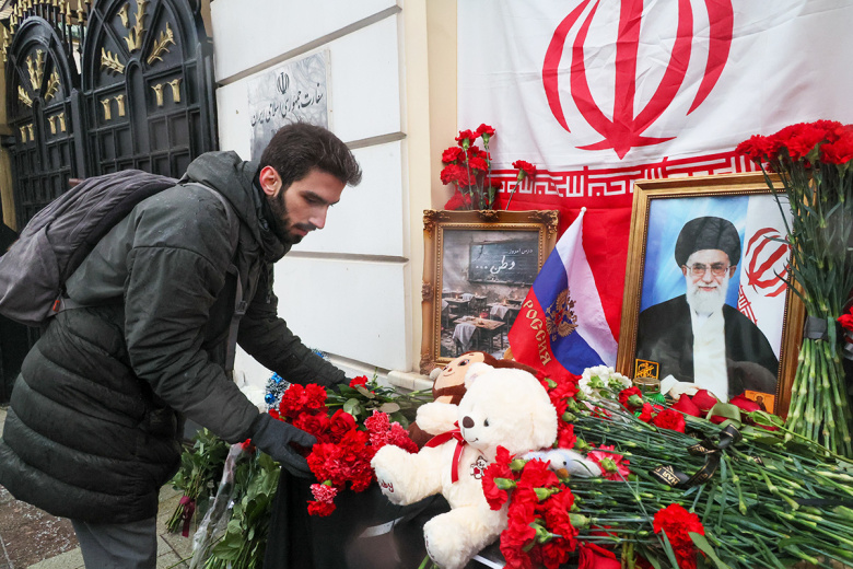 Мужчина возлагает цветы к стихийному мемориалу у посольства Ирана