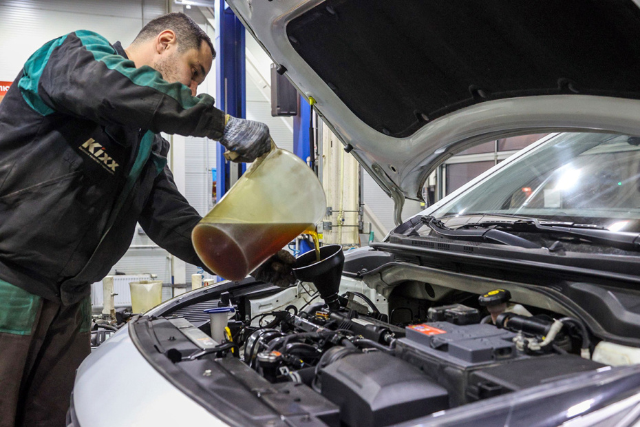 Работник автосервиса заливает масло в двигатель машины