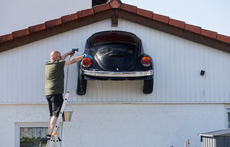 : Мужчина стоит на лестнице и моет припаркованный у дома автомобиль Volkswagen Beetle, Баден-Вюртемберг, Зигмаринген