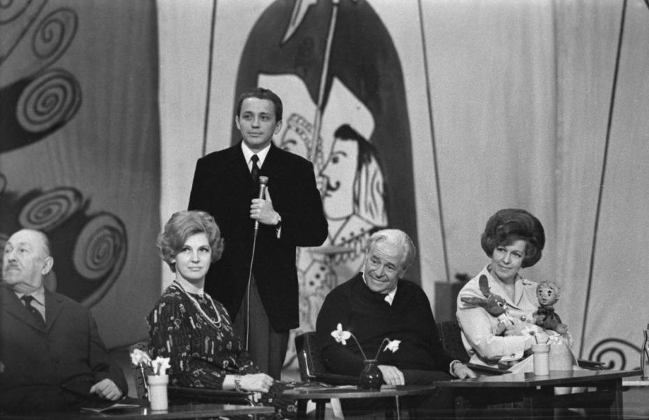 Телевизионная юмористическая игра КВН («Клуб веселых и находчивых»). В центре — ведущий Александр Масляков. Вопросы капитанам задает ведущий телевизионных программ Владимир Адольфович Шнейдеров, 1970 год