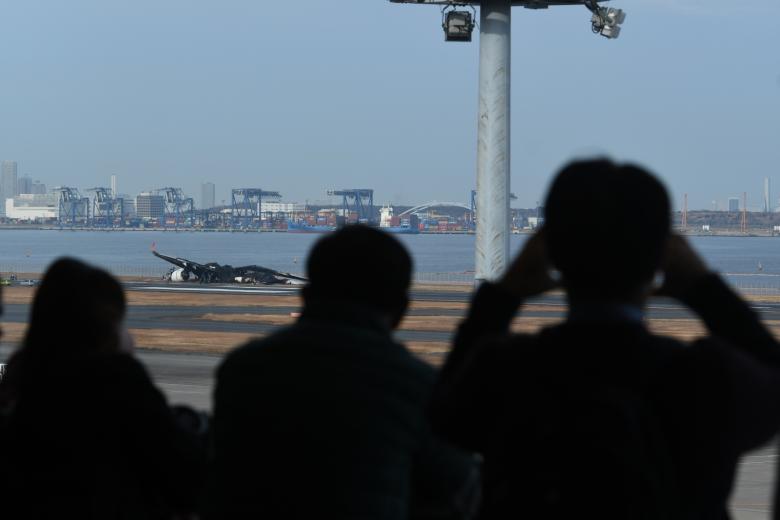 Пассажиры смотрят на обломки рейса 516 JAL после столкновения самолетов в аэропорту Ханэда в Токио