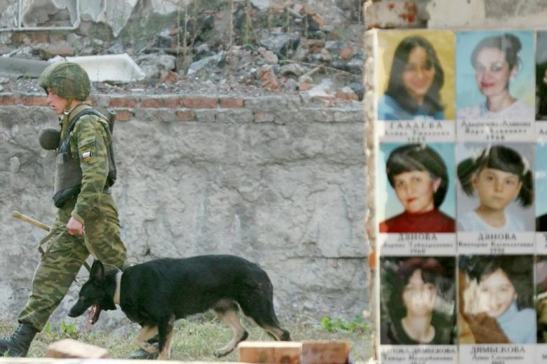 Сотрудник ОМОНа проходит мимо доски с фотографиями жертв захвата школы в 2004 году