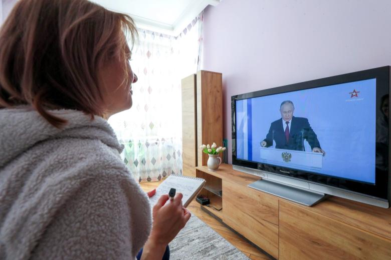 Женщина смотрит трансляцию ежегодного послания президента РФ Владимира Путина Федеральному собранию