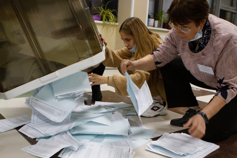 Сотрудники избирательного участка достают из урны бюллетени после завершения голосования