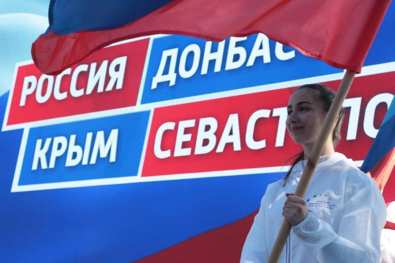 Девушка держит в руках флаг на праздничном митинге в честь восьмилетия провозглашения Донецкой Народной Республики