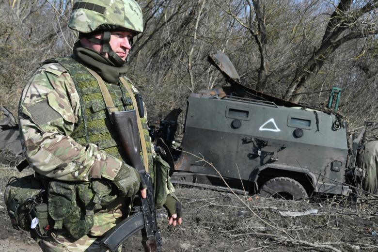 Военнослужащий РФ рядом со сгоревшим бронеавтомобилем ВСУ «Козак» на территории освобожденной деревни Новая Сорочина в Суджанском районе Курской области