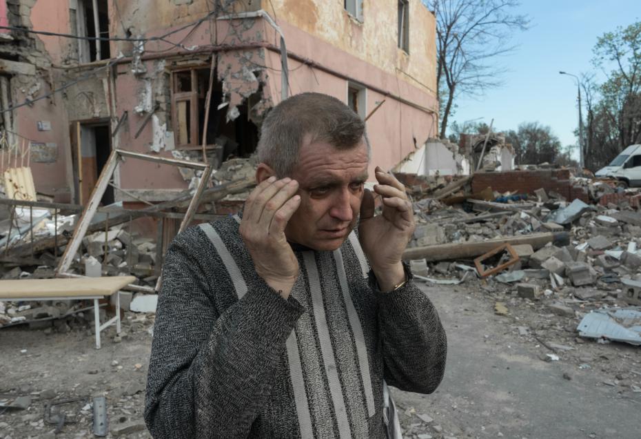 Мужчина около разрушенного здания разбирает вещи под завалом 