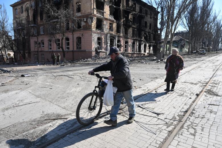 Житель города везёт велосипед на одной из улиц Мариуполя
