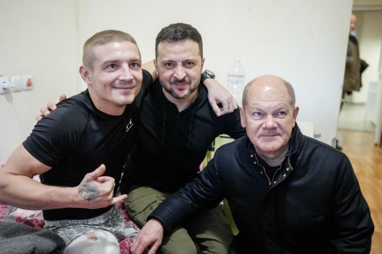 Олаф Шольц (справа) и Владимир Зеленский (в центре), фотографируются с раненым солдатом в больницы Киева