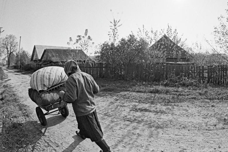 Женщина везёт свои пожитки на тачке по улице села в районе Чернобыльской АЭС