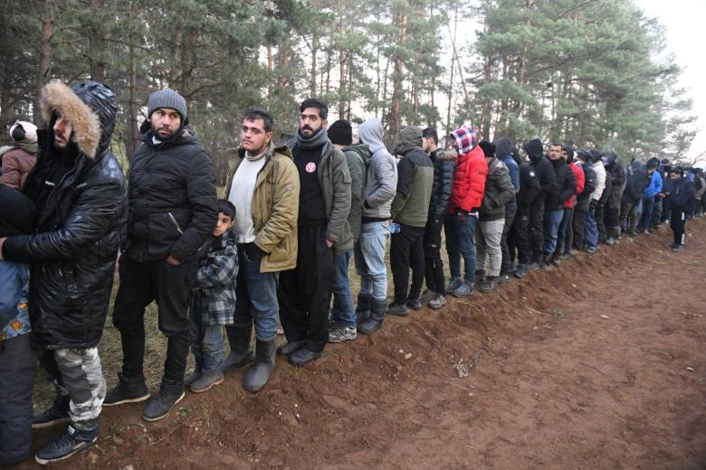 Беженцы стоят в очереди за водой, доставленной волонтёрами, в лагере нелегальных мигрантов на белорусско-польской границе