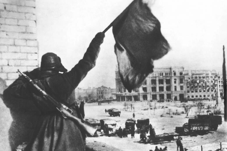 Cолдат Красной армии держит красный флаг над городом как символ победы