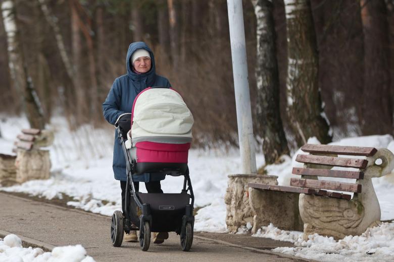 Женщина с детской коляской гуляет весной в парке